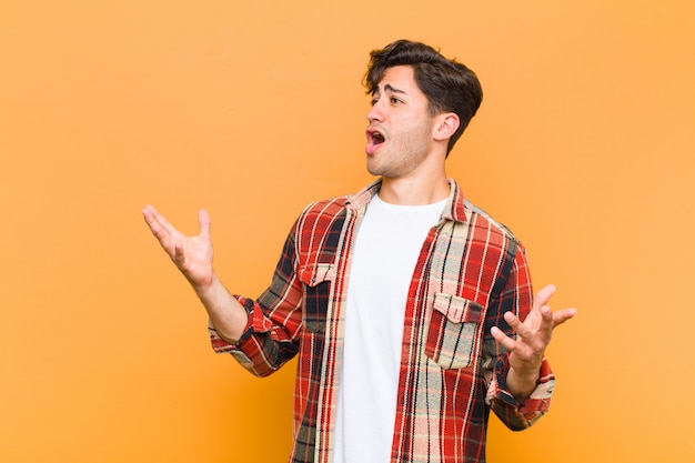 Young handsome man performing opera or singing at a concert or show, feeling romantic, artistic and passionate over orange wall