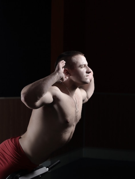 Young handsome man performs sport exercises to strengthen muscles.