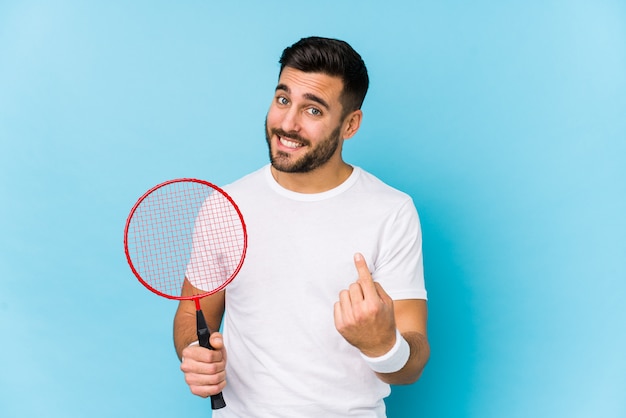 Young handsome man playing badminton isolated pointing with finger at you as if inviting come closer.