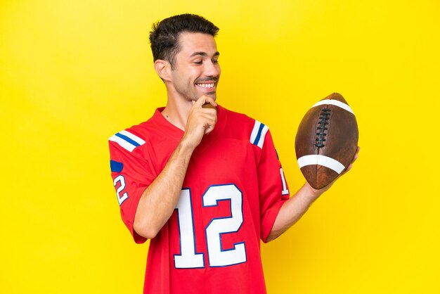 Young handsome man playing rugby over isolated yellow background looking to the side and smiling