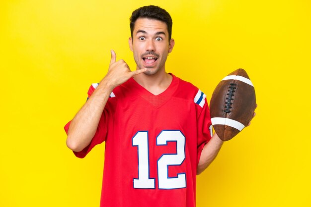 Young handsome man playing rugby over isolated yellow background making phone gesture call me back sign