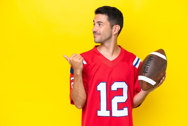 Photo young handsome man playing rugby over isolated yellow background pointing to the side to present a product