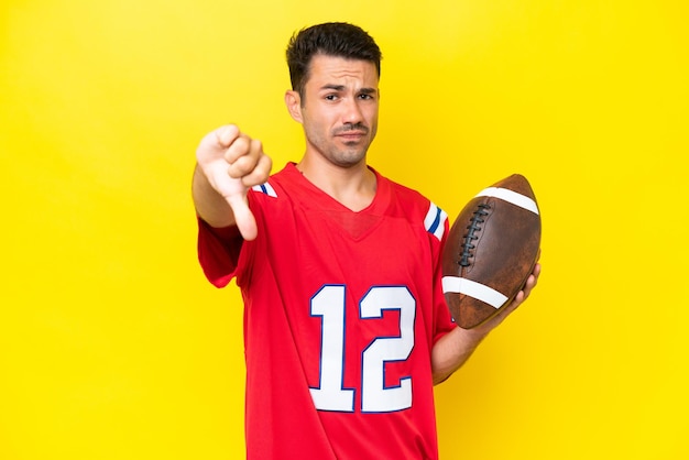 Young handsome man playing rugby over isolated yellow background showing thumb down with negative expression