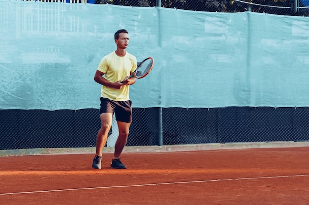 Foto giovane uomo bello che gioca a tennis sul campo da tennis