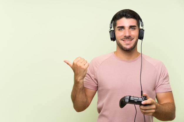 Young handsome man playing with a video game controller over isolated green wall 