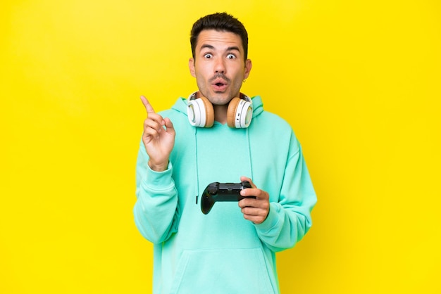 Young handsome man playing with a video game controller over isolated wall intending to realizes the solution while lifting a finger up