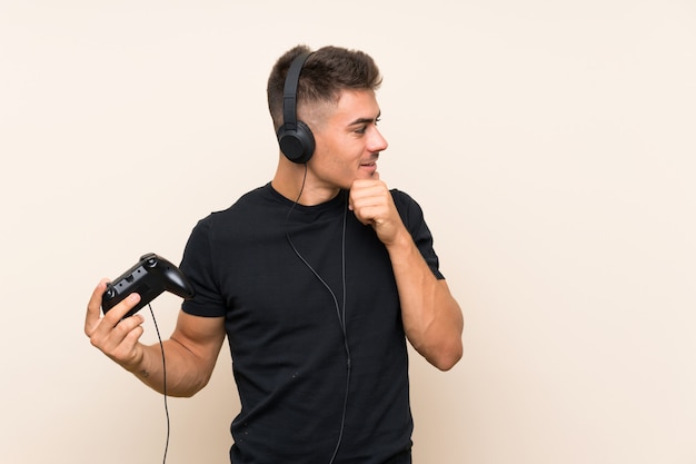 Young handsome man playing with a video game controller over isolated wall thinking an idea and looking side