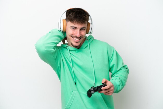 Young handsome man playing with a video game controller isolated on white background laughing