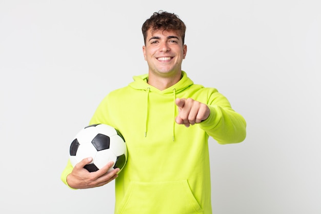 young handsome man pointing at camera choosing you and holding a soccer ball