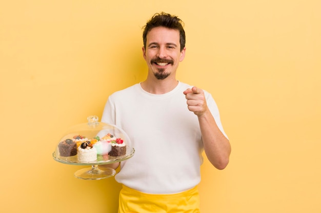 Young handsome man pointing at camera choosing you home made cakes concept