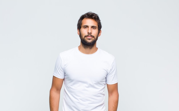 Young handsome man posing and looking to camera against white wall