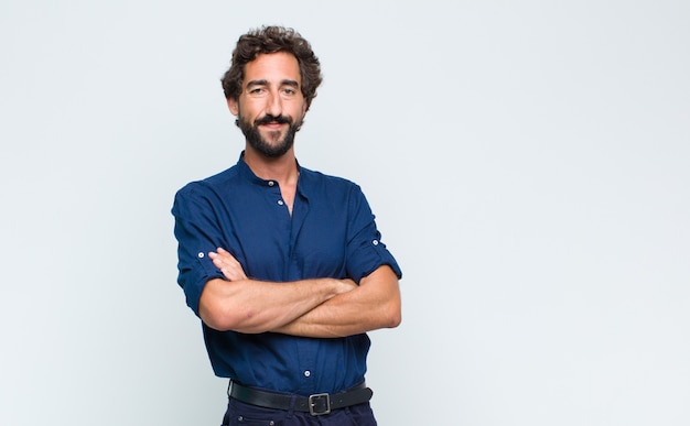 Giovane uomo bello in posa e guardando alla telecamera contro il muro bianco