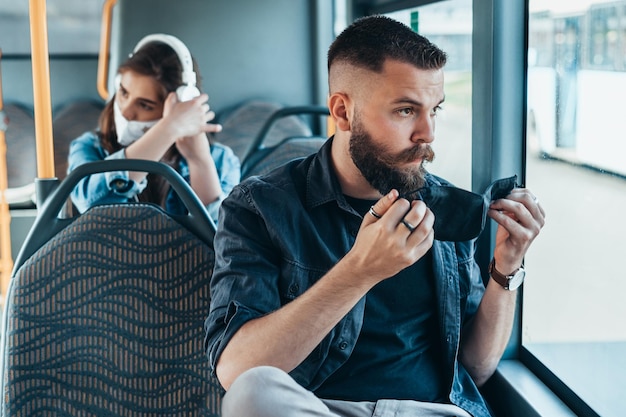 Giovane uomo bello che mette la maschera protettiva in un autobus