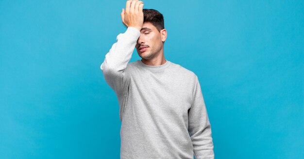 Young handsome man raising palm to forehead thinking oops, after making a stupid mistake or remembering, feeling dumb