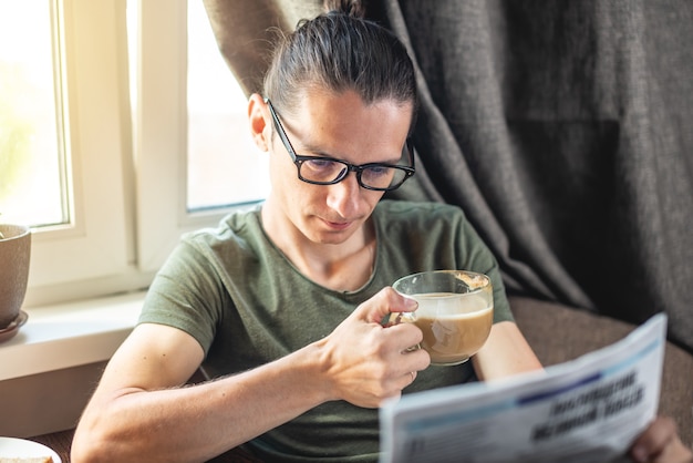 A young handsome man reading interesting hot news articles in a newspaper and drinking Cup of cappuccino