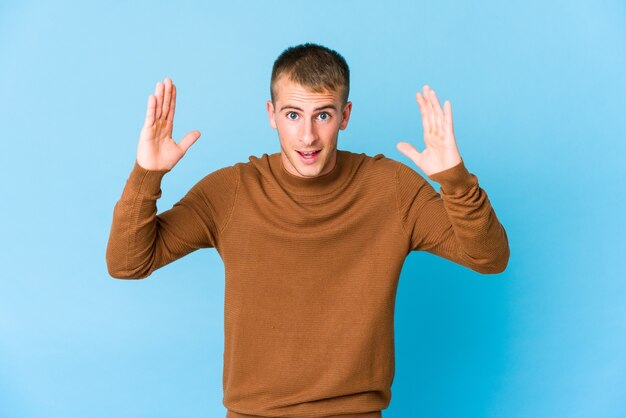 Young handsome man receiving a pleasant surprise, excited and raising hands