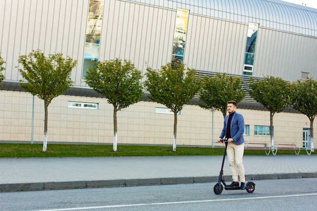 Young handsome man riding the e-scooter on the road near the airport on the sunset