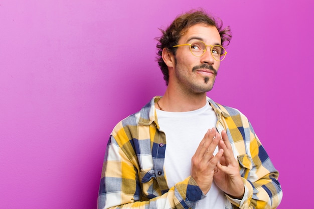 Young handsome man scheming and conspiring, thinking devious tricks and cheats, cunning and betraying against purple wall