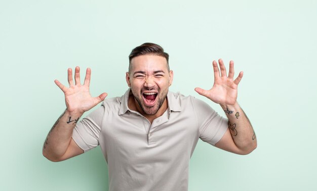 Young handsome man screaming in panic or anger shocked terrified or furious with hands next to head