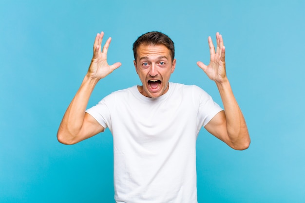 Young handsome man screaming with hands up in the air, feeling furious, frustrated, stressed and upset