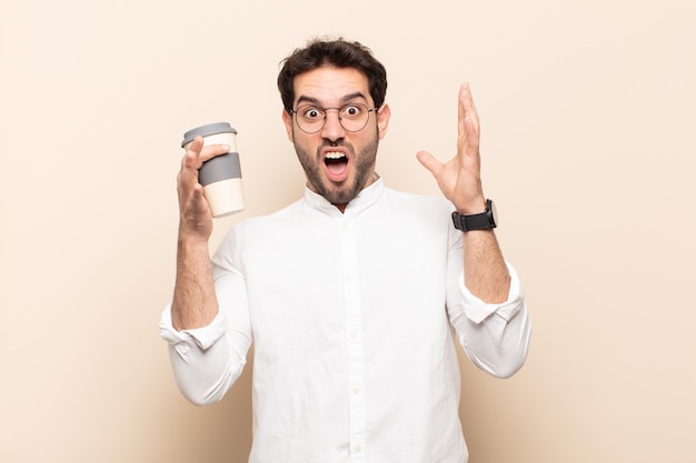 Young handsome man screaming with hands up in the air, feeling furious, frustrated, stressed and upset