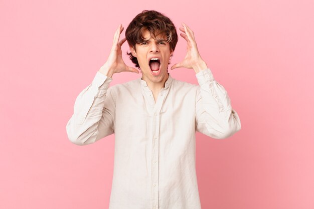 Young handsome man screaming with hands up in the air