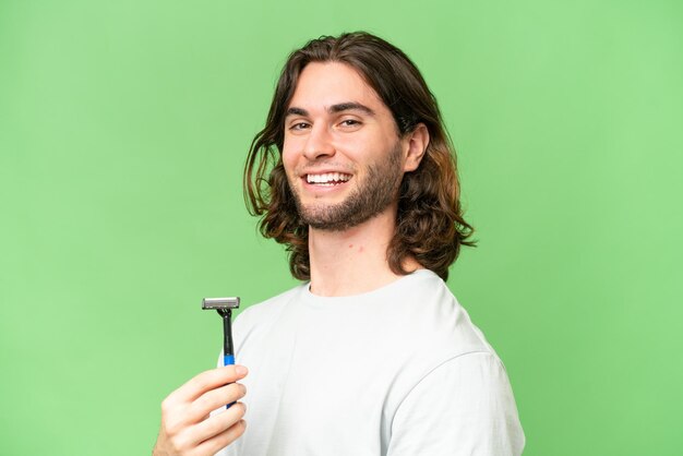 Young handsome man shaving his beard over isolated background smiling a lot