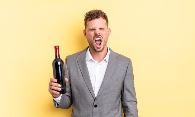 Young handsome man shouting aggressively, looking very angry. bottle of wine concept