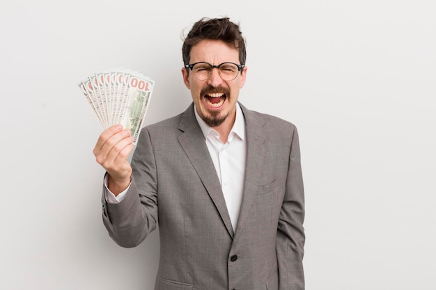 Young handsome man shouting aggressively looking very angry businessman and banknotes