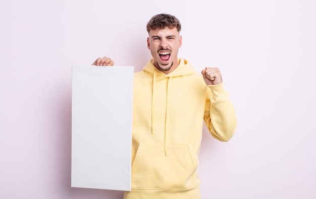 Young handsome man shouting aggressively with an angry expression. blank canvas concept