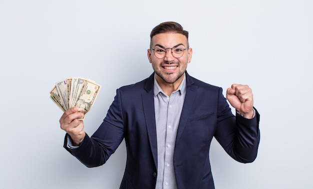 Young handsome man shouting aggressively with an angry expression. dollar banknotes concept