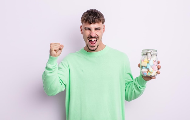 Young handsome man shouting aggressively with an angry expression jelly candies concept