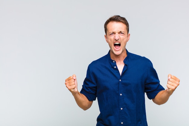 Young handsome man shouting aggressively with an angry expression or with fists clenched celebrating success