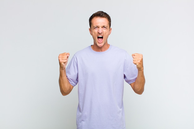 Young handsome man shouting aggressively with an angry expression or with fists clenched celebrating success