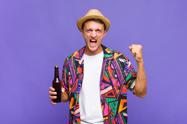 Young handsome man shouting aggressively with an angry expression or with fists clenched celebrating success