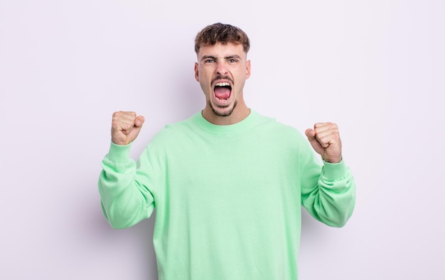 Young handsome man shouting aggressively with an angry expression or with fists clenched celebrating success