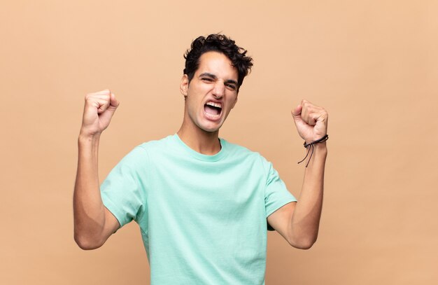 Young handsome man shouting triumphantly, looking like excited, happy and surprised winner, celebrating