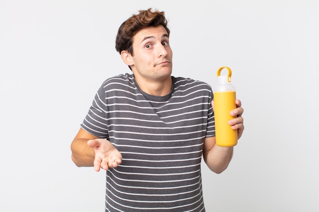 Young handsome man shrugging, feeling confused and uncertain and holding a coffee thermos