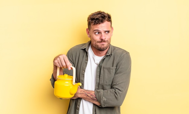 Young handsome man shrugging, feeling confused and uncertain. teapot concept