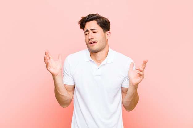 Young handsome man shrugging with a dumb, crazy, confused, puzzled expression, feeling annoyed and clueless against pink background