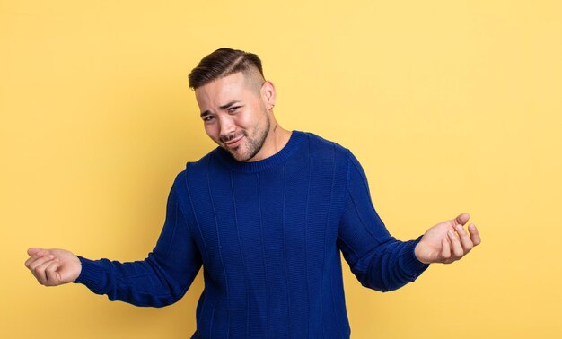 Young handsome man shrugging with a dumb, crazy, confused, puzzled expression, feeling annoyed and clueless