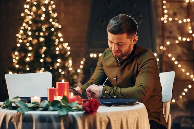 Young handsome man sits by the table and waits for girlfriend for romantic dinner in restaurant