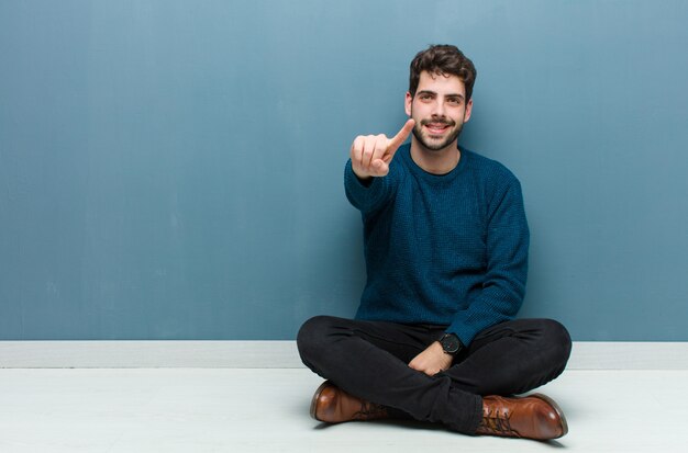 Young handsome man sitting on floor feeling happy and successful, smiling and clapping hands, saying congratulations with an applause