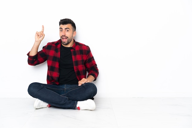 Young handsome man sitting on the floor intending to realizes the solution while lifting a finger up