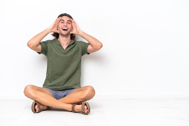 Young handsome man sitting on the floor isolated on white background with surprise expression