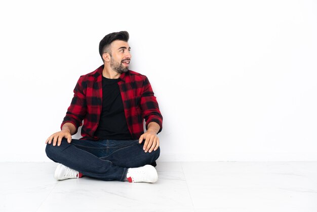 Photo young handsome man sitting on the floor laughing in lateral position