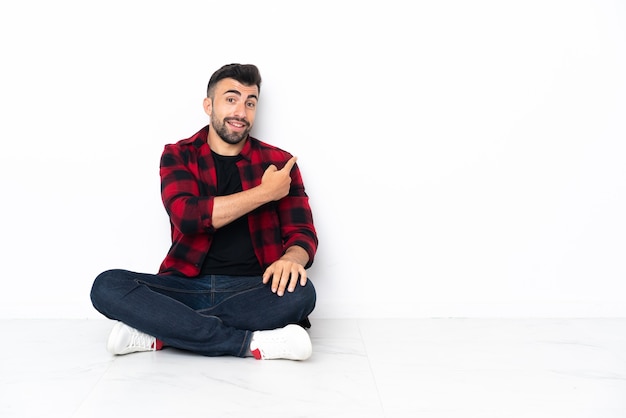 Young handsome man sitting on the floor pointing back