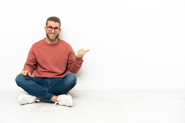 Young handsome man sitting on the floor pointing to the side to present a product