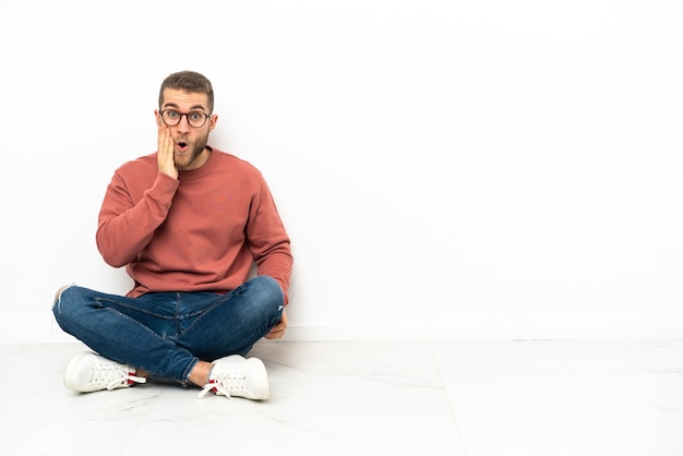 Young handsome man sitting on the floor with surprise and shocked facial expression