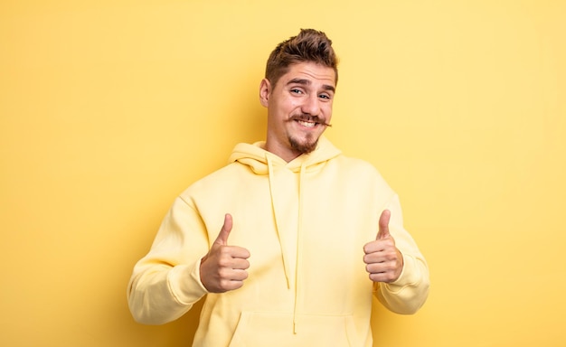 Young handsome man smiling broadly looking happy, positive, confident and successful, with both thumbs up. strange moustache concept